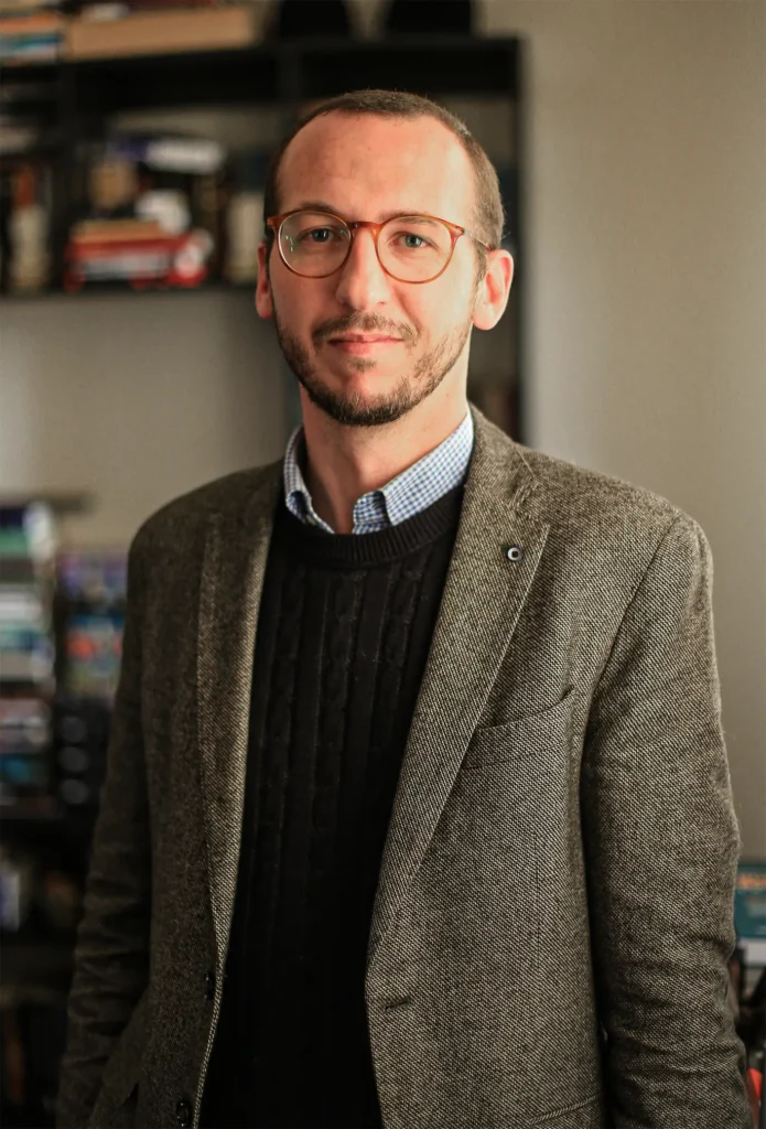 Professor Deividi Pansera em seu escritório, diante de uma estante de livros
